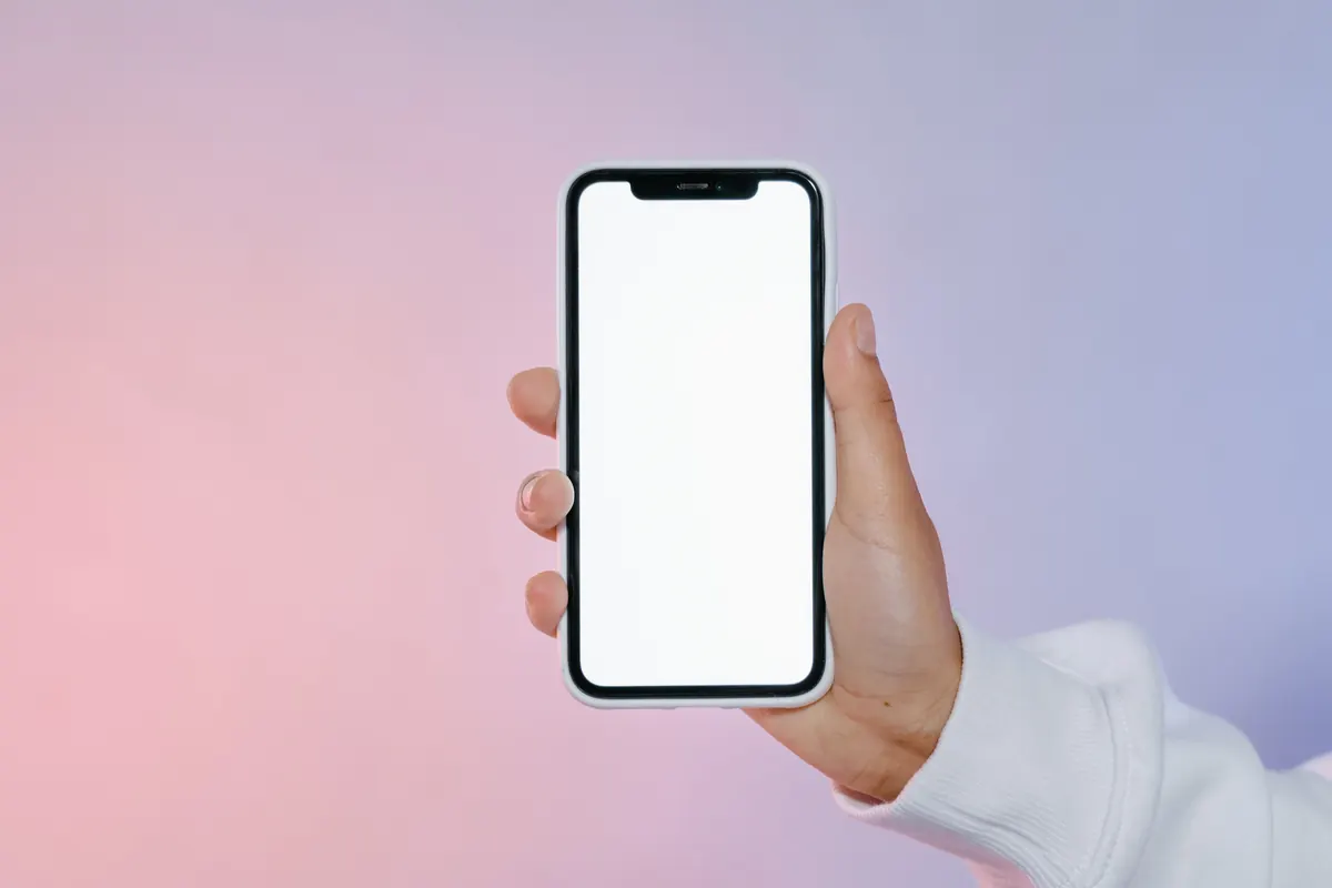 Hand holding a blank-screen phone against a pink and purple background.