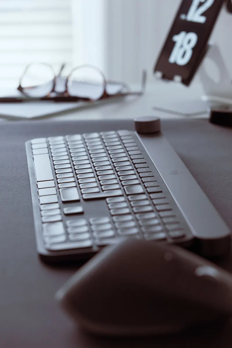 Keyboard and mouse on a desk with a blurred clock in the background.