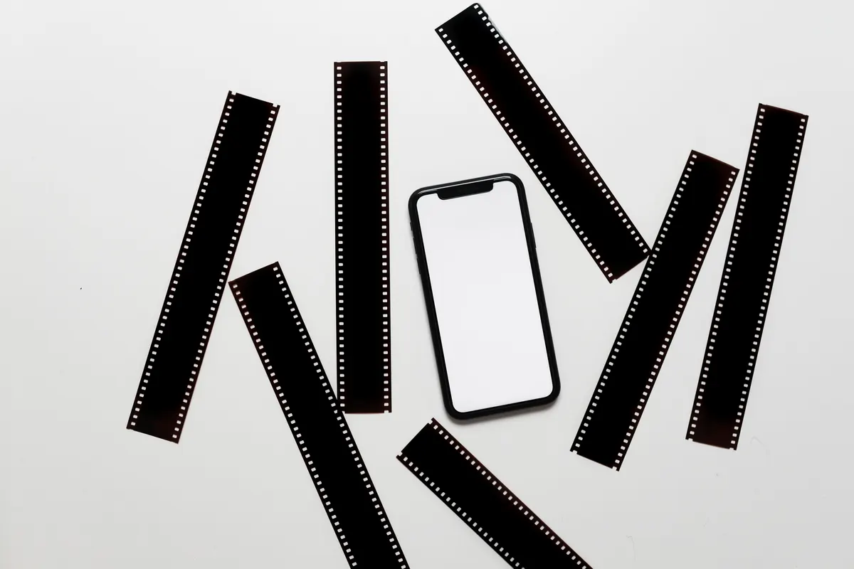 Blank-screen phone surrounded by dark filmstrips on a pale surface.