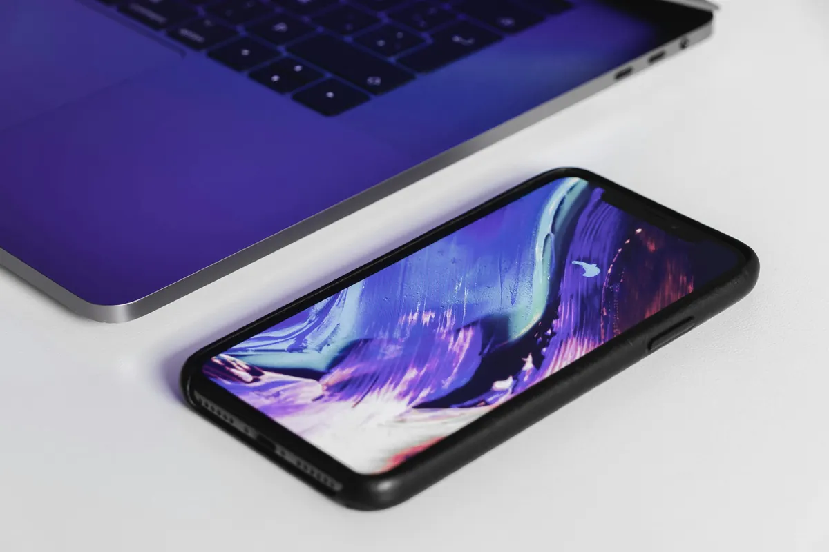 A smartphone with a colorful abstract wallpaper lying beside the edge of an open laptop.