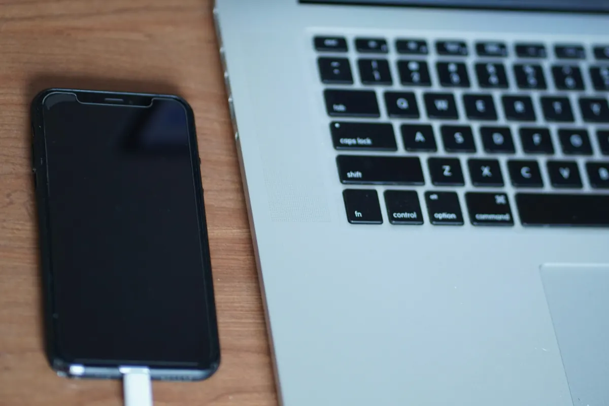A smartphone with a dark screen plugged into a cable next to a laptop keyboard.