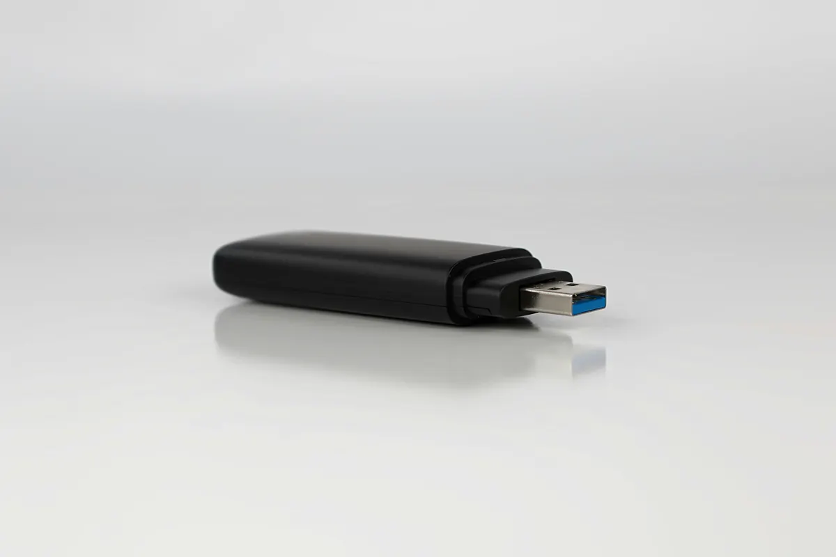 A plain black USB flash drive lying on a white surface.
