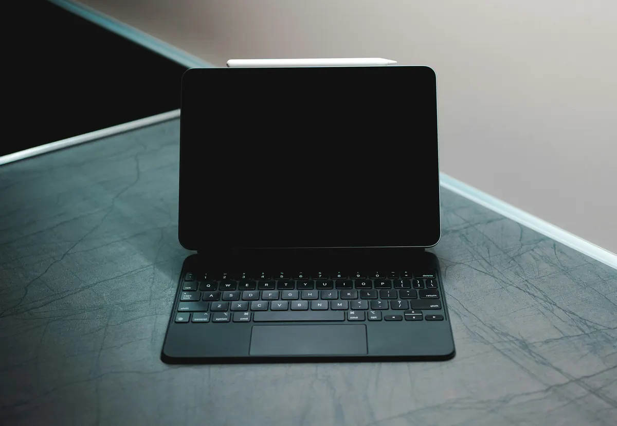 A tablet with a dark screen attached to a black keyboard case on a gray surface.